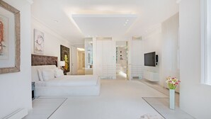 A spacious hotel bedroom with a large bed, a TV, and a bathroom visible through an open door. - The White Peace Garden 3 bed Hampstead - by Out of Office Lifestyle (London)