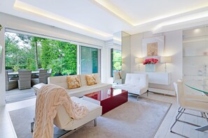 A modern living room with a white sofa, a red coffee table, and a glass dining table. - The White Peace Garden 3 bed Hampstead - by Out of Office Lifestyle (London)