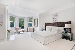A spacious bedroom with a large bed, a desk, and a chair, all in a modern white design. - The White Peace Garden 3 bed Hampstead - by Out of Office Lifestyle (London)