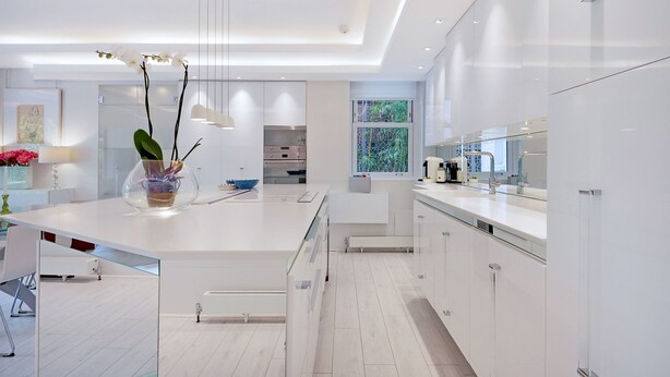 A modern kitchen with white cabinetry, a central island, and a large window providing natural light. - The White Peace Garden 3 bed Hampstead - by Out of Office Lifestyle (London)