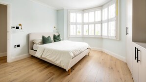 A bedroom with a bed, a window with blinds, a bedside lamp, and a wardrobe. - The Blooming Minimalist- by Out of Office Lifestyle (London)