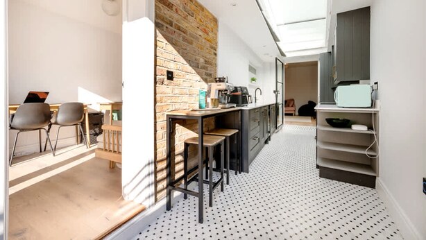 A modern kitchen with a brick wall, a dining area with chairs, and a kitchen island. - The Blooming Minimalist- by Out of Office Lifestyle (London)