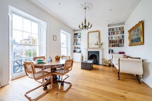 A spacious room with a large dining table, chairs, a chandelier, bookshelves, a fireplace, and a view through a large window. - Highlife and Islington - by Out of Office Lifestyle (London)