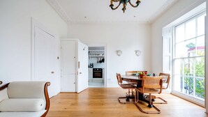 A spacious room with a wooden floor, a dining area with a table and chairs, a sofa, and a view of a balcony through a large window.