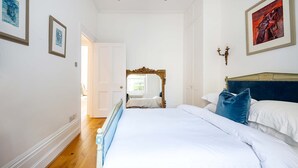 A bedroom with a large bed, a wooden floor, a white door, and a painting on the wall.