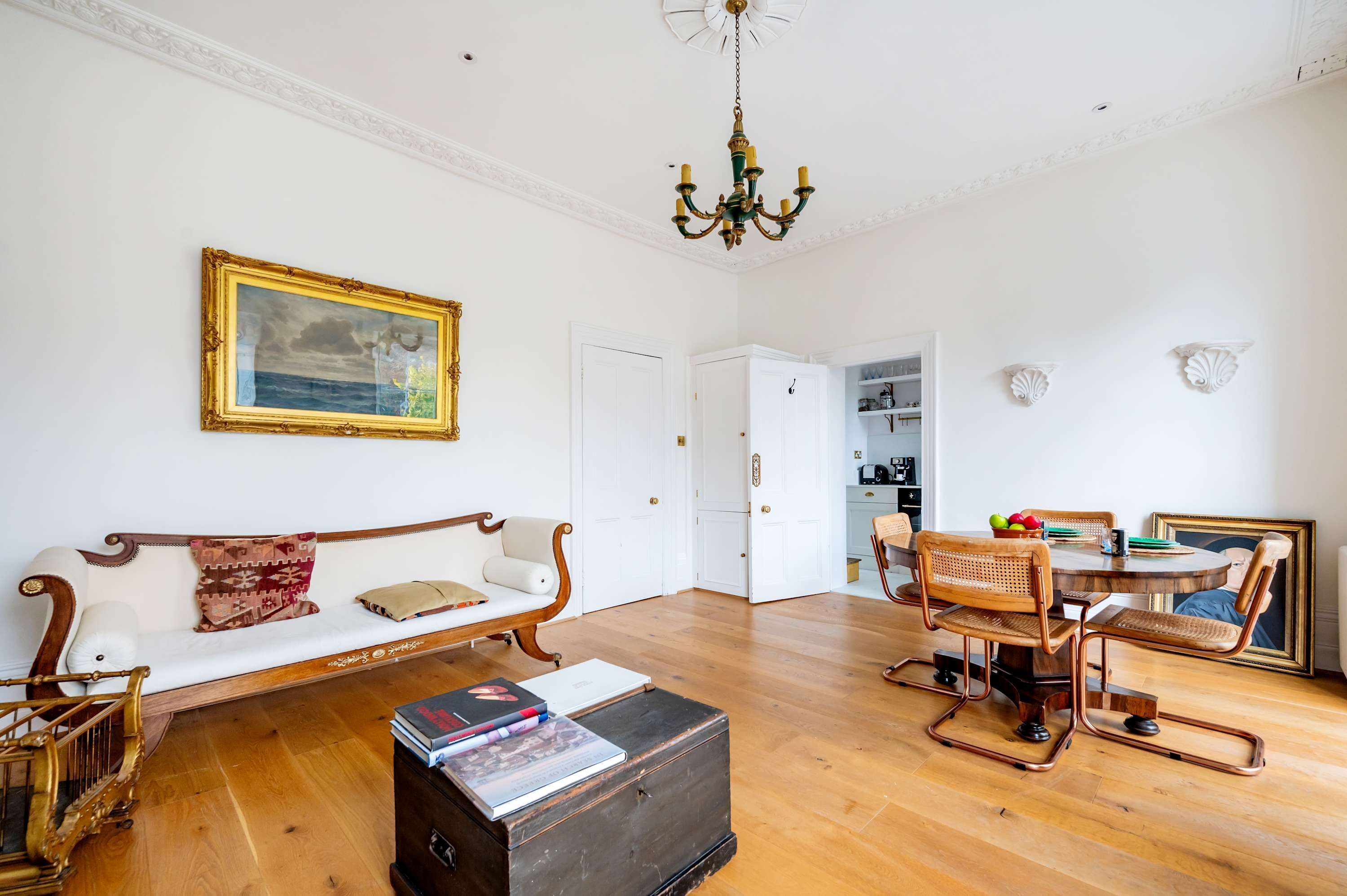 A spacious living room with a wooden floor, a white sofa, a dining table with wicker chairs, and a chandelier.