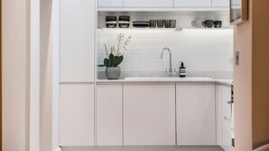 Une cuisine moderne avec des meubles blancs, un évier en acier inoxydable et une orchidée en pot posée sur le plan de travail.
