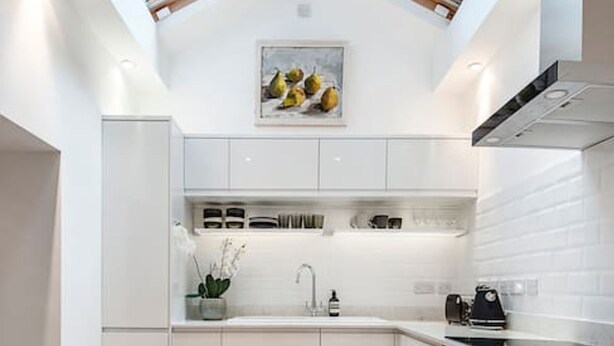 Une cuisine moderne avec des meubles blancs, un puits de lumière et un sol carrelé.