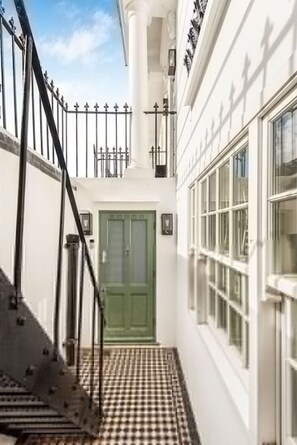 A narrow hallway with a checkered floor, a green door, and a white building with large windows. - Miss Westside Story - by Out of Office Lifestyle (London)