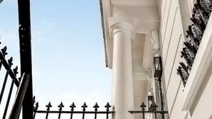 Un bâtiment aux colonnes blanches, un balcon orné de balustrades travaillées et un ciel dégagé.