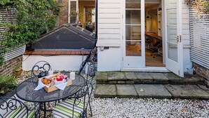 A courtyard with a metal table and chairs, a small garden area, and a building with a white door and windows.