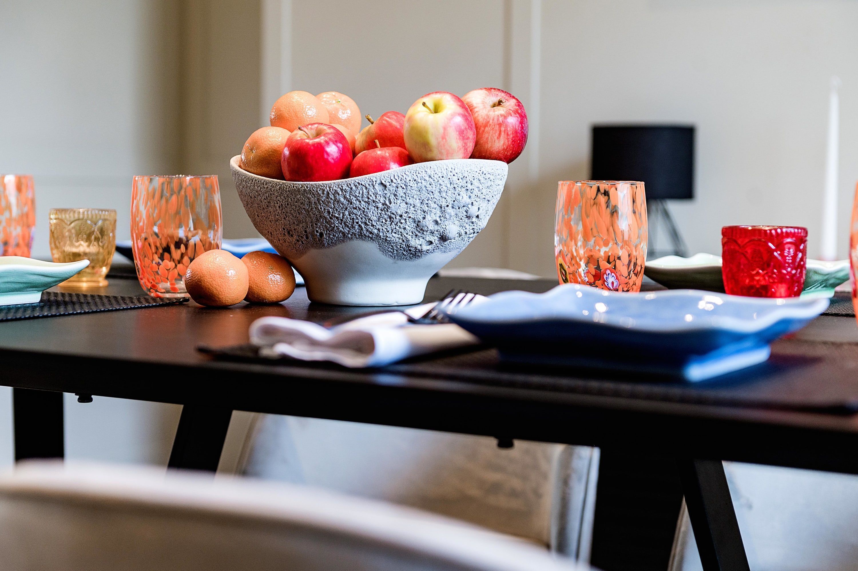 A dining table with a bowl of fruit, a plate, and a napkin.