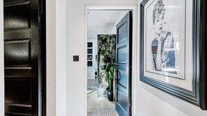 A hallway with a dark wooden door, a framed artwork, and a potted plant. - Notting Hill 2 Bed With Sauna - by Out of Office Lifestyle (London)