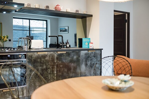 Una cocina moderna con una isla central, una zona de comedor con mesa y sillas, y vistas a través de un ventanal.