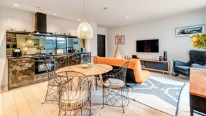 A modern kitchen with a dining area, a sofa, and a TV. - Notting Hill 2 Bed With Sauna - by Out of Office Lifestyle (London)