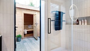 A modern bathroom with a glass shower enclosure, wooden sauna, and a small shelf with toiletries. - Notting Hill 2 Bed With Sauna - by Out of Office Lifestyle (London)