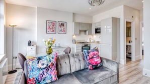 A modern living room with a grey sofa, colorful cushions, a vase with flowers, and a chandelier.