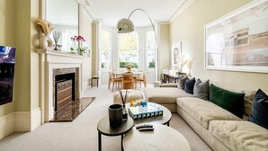 A living room with a fireplace, a sofa, a coffee table, and a dining area with chairs and a table. - Kensington High Life- by Out of Office Lifestyle (London)