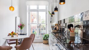 A modern kitchen with a large window, white cabinets, and pendant lighting. - Lady on the Lane- 2 bed Primrose Hill - by Out of Office Lifestyle (London)