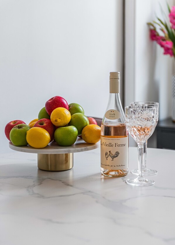 Une table en marbre ornée d’un arrangement de fruits, une bouteille de vin et un verre.