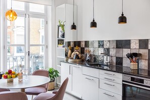 A modern kitchen with white cabinets, a black countertop, and hanging pendant lights. - Lady on the Lane- 2 bed Primrose Hill - by Out of Office Lifestyle (London)