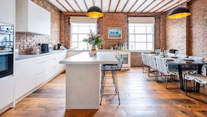 A spacious kitchen with a large island, wooden flooring, and exposed brick walls. - Long Term Stay- Notting Hill by Out of Office Lifestyle (London)