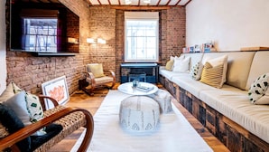 A cozy living room with exposed brick walls, a wooden ceiling, a sofa set, a coffee table, and a fireplace. - Long Term Stay- Notting Hill by Out of Office Lifestyle (London)
