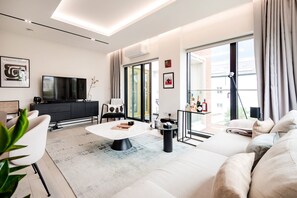 A modern living room with a sofa, coffee table, and TV. There is a balcony with a view of the city. - The Modern Glasshouse - by Out of Office Lifestyle (London)