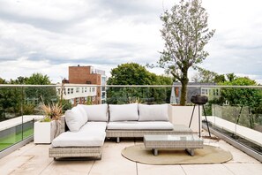 A rooftop terrace with a modern outdoor sofa, a small table, and a potted plant. - The Modern Glasshouse - by Out of Office Lifestyle (London)