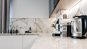A modern kitchen with a marble backsplash, a coffee maker, and a kettle.