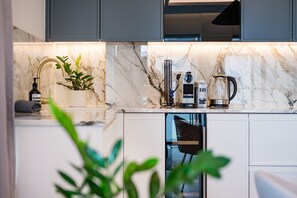 A modern kitchen with marble countertops, a built-in coffee maker, and a plant. - The Modern Glasshouse - by Out of Office Lifestyle (London)