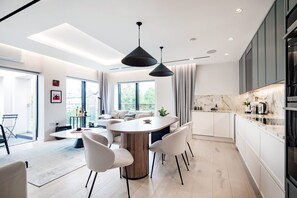 A modern kitchen with a marble countertop, pendant lighting, and a dining area with a round table and chairs. - The Modern Glasshouse - by Out of Office Lifestyle (London)