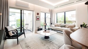 A modern living room with a sofa, armchairs, a coffee table, and large windows offering a view of the outdoors.