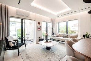 A modern living room with a sofa, armchairs, a coffee table, and large windows offering a view of the outdoors. - The Modern Glasshouse - by Out of Office Lifestyle (London)
