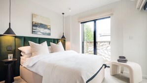 A modern bedroom with a large bed, two bedside tables, a bench, a painting, and a view of greenery through the window.