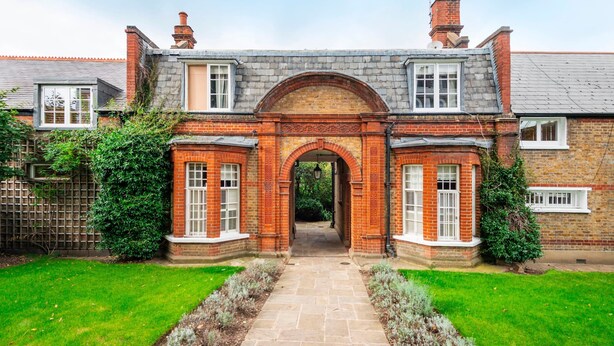 A traditional brick house with a central archway, a stone pathway leading to the entrance, and a well-maintained garden. - The Kensington Gatehouse - by Out of Office Lifestyle (London)
