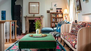 A cozy living room with a green ottoman, a striped sofa, a bookshelf, and a fireplace. - The Kensington Gatehouse - by Out of Office Lifestyle (London)