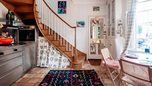 A kitchen with a wooden staircase, a dining area with a table and chairs, and a view of the outdoors through a window. - The Kensington Gatehouse - by Out of Office Lifestyle (London)