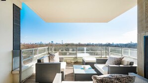 A balcony with wicker furniture, a glass railing, and a city view. - Regents Park Penthouse (London)