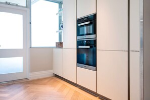 A kitchen with white cabinets, a built-in oven, and a window with a view. - Regents Park Penthouse (London)