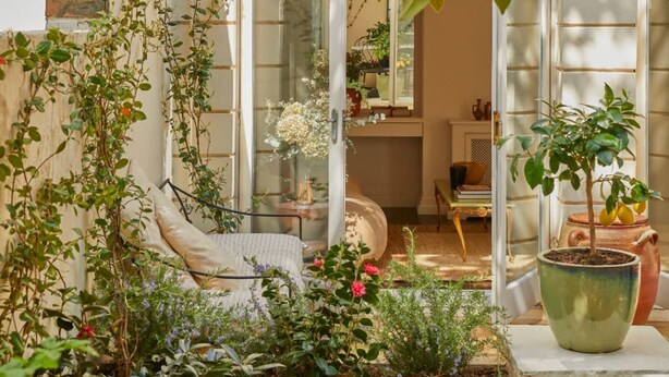 Un jardín acogedor con un muro de ladrillo, una silla blanca y diversas plantas.