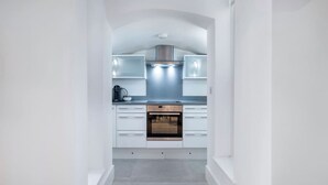 A narrow, white-walled kitchen with a built-in oven and a stainless steel range hood. - The Urban Minimalist- Notting Hill 2 Bed (London)