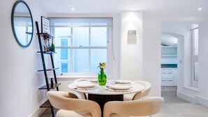 A modern dining area with a round table, four chairs, a green vase, and a ladder shelf against a white wall. - The Urban Minimalist- Notting Hill 2 Bed (London)