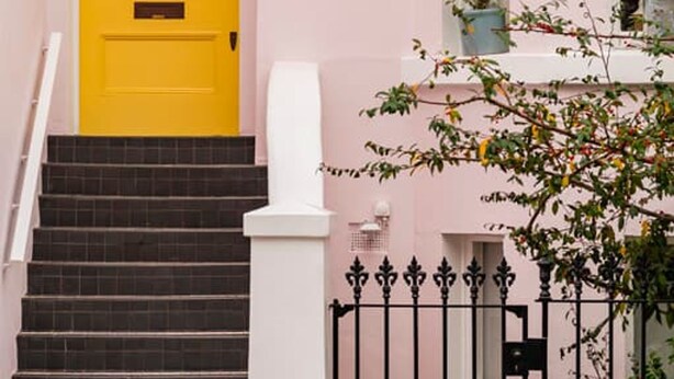 A pink building with a bright yellow door, a staircase, and a white railing. - The Urban Minimalist- Notting Hill 2 Bed (London)