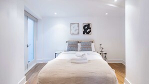 A modern bedroom with a large bed, two pillows, a bedside table, and a nightstand. - The Urban Minimalist- Notting Hill 2 Bed (London)