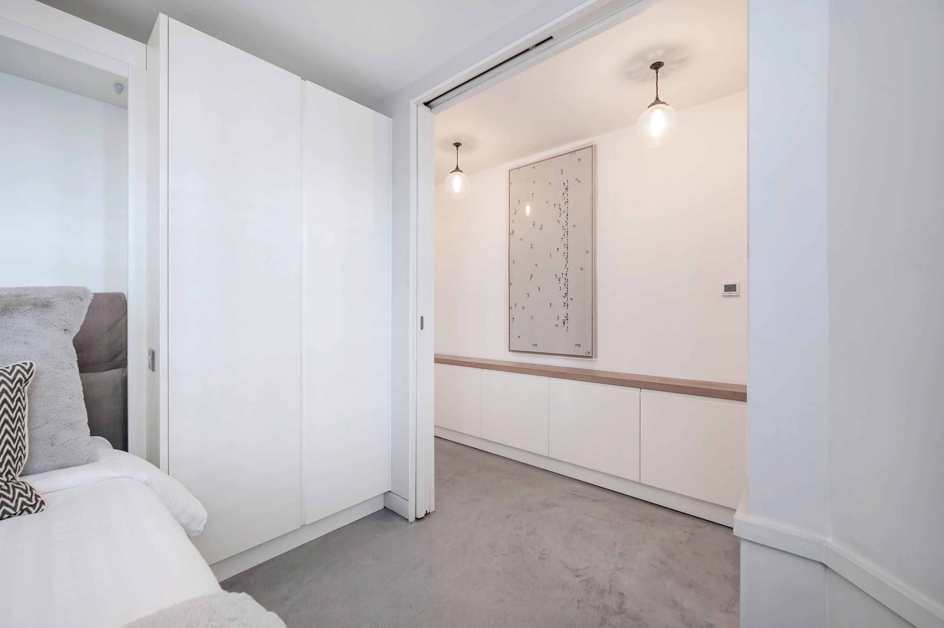 Un dormitorio con cama, un armario, un pasillo con lámpara y una luz empotrada en la pared.