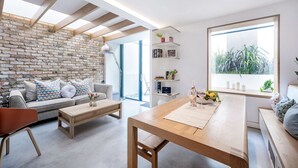 Una sala de estar moderna con una pared de ladrillo, un sofá, una mesa de centro de madera y un ventanal con plantas.
