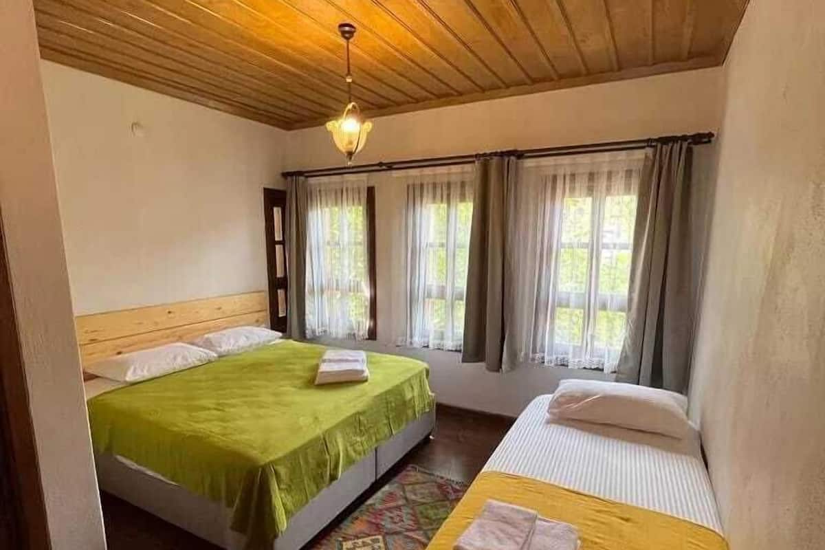 A room with two beds, wooden ceiling, and large windows with curtains.