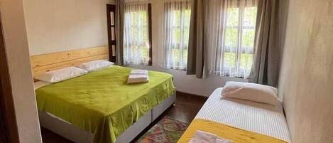 A room with two beds, wooden ceiling, and large windows with curtains.
