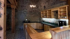 A rustic kitchen with exposed wooden beams, a stone wall, and a curved wooden countertop. - Trilye Taşev (Mudanya)
